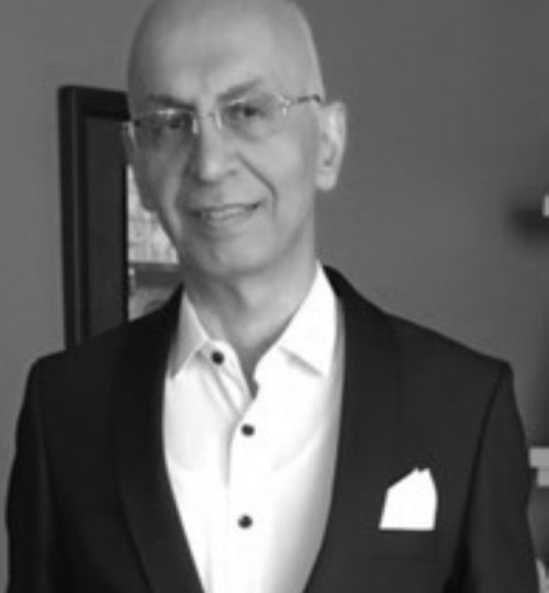 A smiling man in a suit and glasses posing indoors.