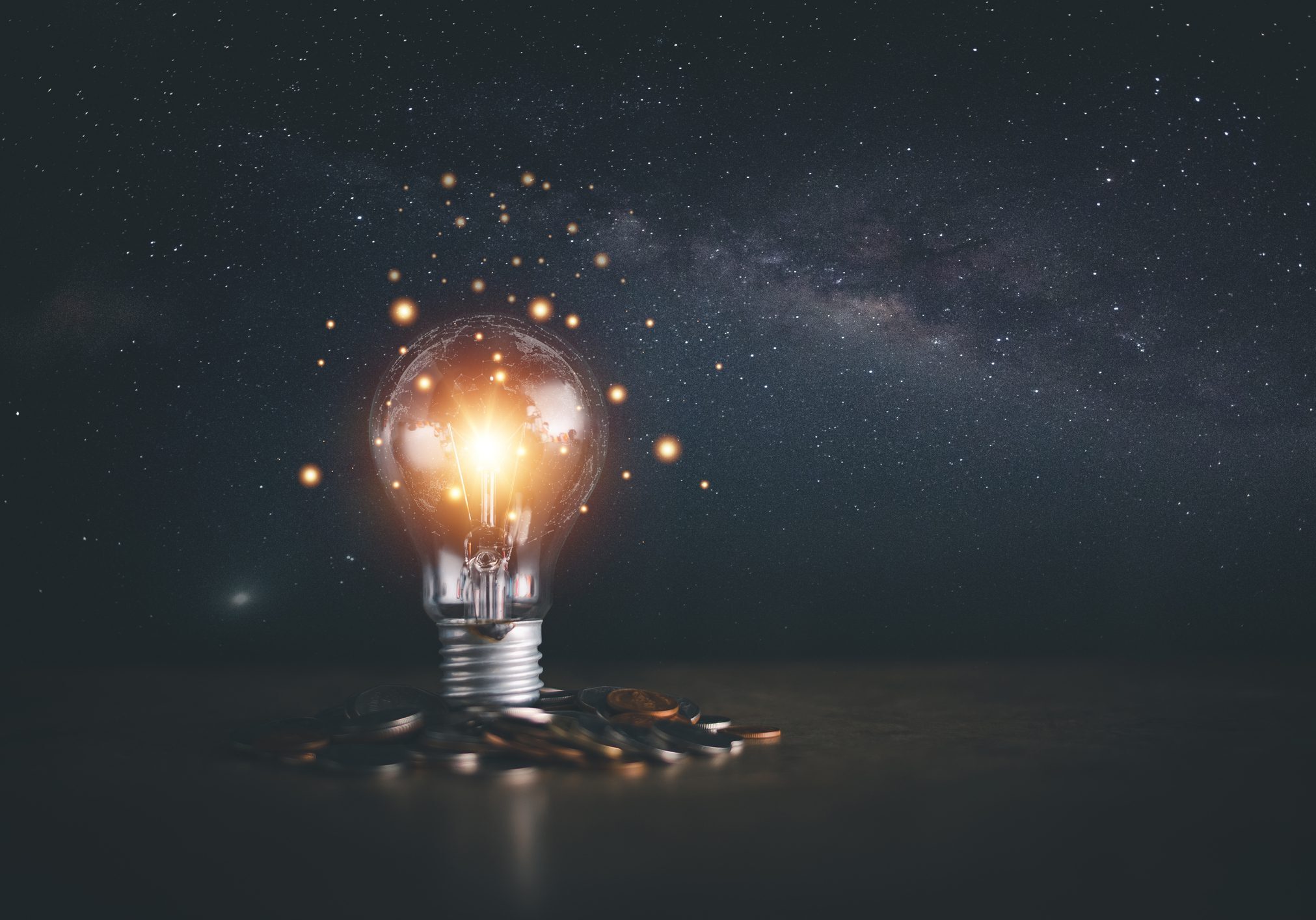 Light bulb glowing with stars inside under a starry sky.